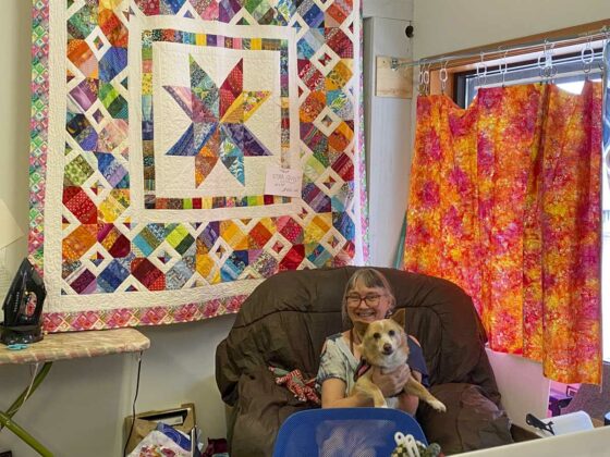 Mary Anderson and friend sit vigil in front of her fibre art offerings.