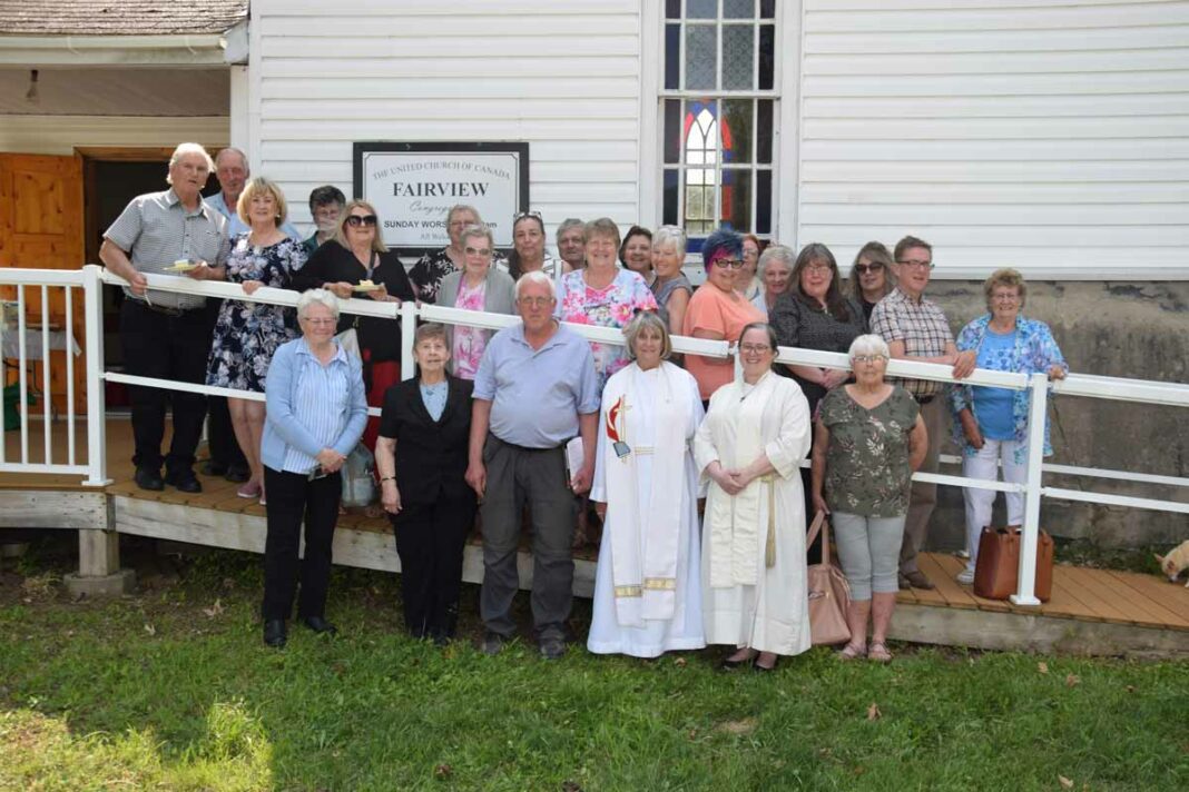 June McDougall, centre left in robes (who also officiates at Knox United Church in Manitowaning and St. Andrews by the Sea in South Baymouth) and Rev. of Melody Duncanson-Hales, Canadian Shield Region support minister are joined by many of the members of the Fairview United Church in Tehkummah in front of the building following its decommissioning as a church. There were considerably more in attendance for the final service, but who declined taking part in the photograph. photo by Michael Erskine