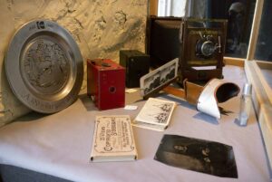 Cabinet of curiosities: Featured in this display are a Kodak 100th Anniversary plate (rear); at right, a large Eastman 5x7” view camera made by Eastman Kodak Co. (1914-1925) from the Marshall family, Manitoulin; two box cameras, centre, a Kodak Brownie No.2A model B (1909-1917) and a Kodak Brownie No.2A model C (1920-24); the stereoscope and stereo cards were popular in the 1880s to early 1900s.