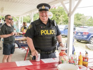 OPP Community Services Officer Constable Al Boyd, pauses “in a very busy weekend talking to the public and providing a presence” to grab a bite and cool off with a cold soda at the fundraising barbecue.