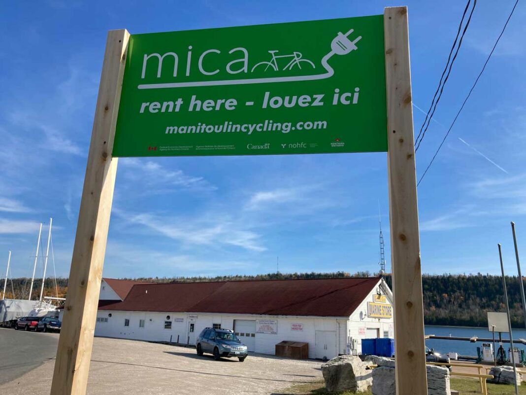 MICA e-bike rental locations (listed on the MICA website) are found near bright green signs like this one at the Gore Bay Marina. Photo by Isobel Harry.