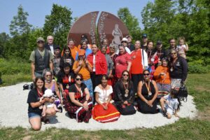 Family members of Murdered and Missing Indigenous Women, Girls and Two-Sprited+ gather with knowledge-keepers and dignitaries in front of the new monument at Whitefish River First Nation. The monument, created from a massive chunk of stone imported from India features the carved image of a jingle dancer, carved flowers and strawberries and a drum. The five-inch gap in the stone symbolizes the missing and the circle that can never be complete. photo by Michael Erskine