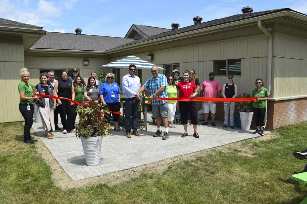 Mnaamodzawin Health Services Inc. executive director Craig Abotossaway and board chair Kevin Mossip cut the ribbon outside on the new patio that is part of the organization’s expansion while staff members stand behind them. photo by Michael Erskine