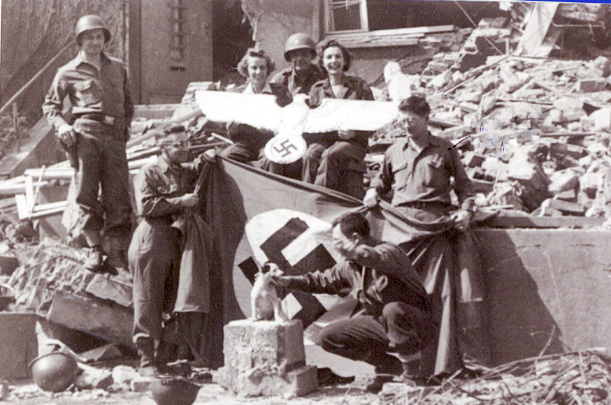 Blair holding the left end of the German flag. He found the small dog in a house and carried it with him in his jacket until the end of the war.