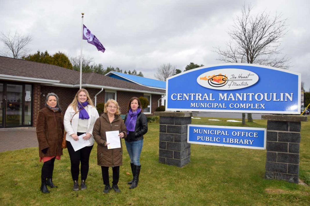 Supervisor Marissa McCready, Central Manitoulin CEO Ruth Frawley and MFR Executive Director Marnie Hall raise a purple flag at the Central Manitoulin municipal office.