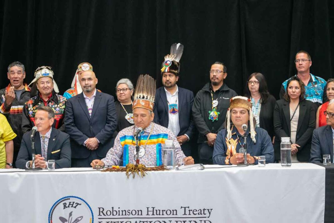 The speakers at the proposed settlement announcement included, from left, Ontario Indigenous Affairs Minister Greg Rickford, Batchewana First Nation Chief Dean Sayers, and Robinson-Huron Treaty Litigation Fund trustee Duke Peltier. They are joined by several Manitoulin Island chiefs on hand for the historic announcement. photo by Warren Schlote