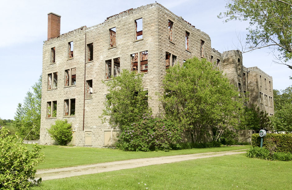 SOMBRE MONUMENT––The decaying hulk of St. Joseph School for Girls near Spanish. The residential school building, now private property, ceased to function as a school in 1962. Later, it became an apartment building, suffered a fire that left fatalities and remains as it is seen in this recent photo. The inscription, below, is on the back of a memorial stone on the old Garnier School site. photos by Expositor staff