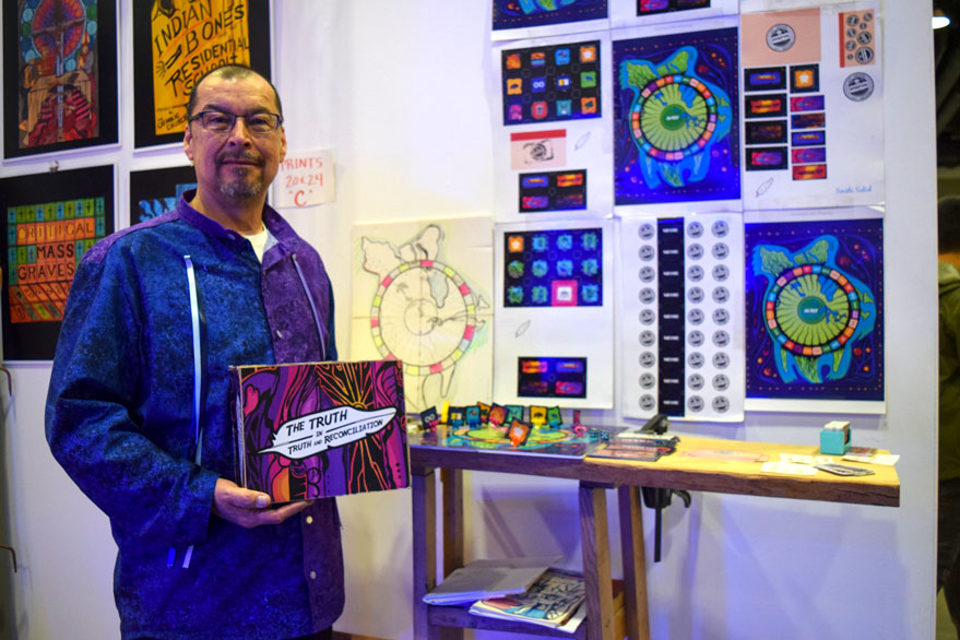 James Darin Corbiere of Wiikwemkoong poses with his board game prototype, the Truth in Truth and Reconciliation Game.