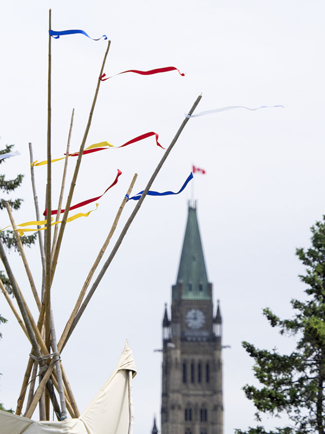 A tipi on Victoria Island reaches for the sky along with the Peace Tower on Parliament Hill in the background. 