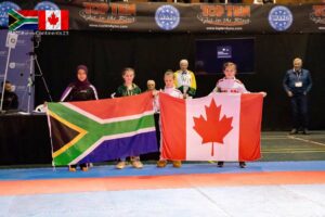 Olivia, third from left, holds up one end of the Canadian flag during the taekwondo tournament in South Africa. South Africa’s flag is to the left.