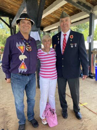 A rose betwween? Co-MC Duke Peltier, left, and head veteran Wayne Pitwawakwat join Bonnie Kogos for a photo.