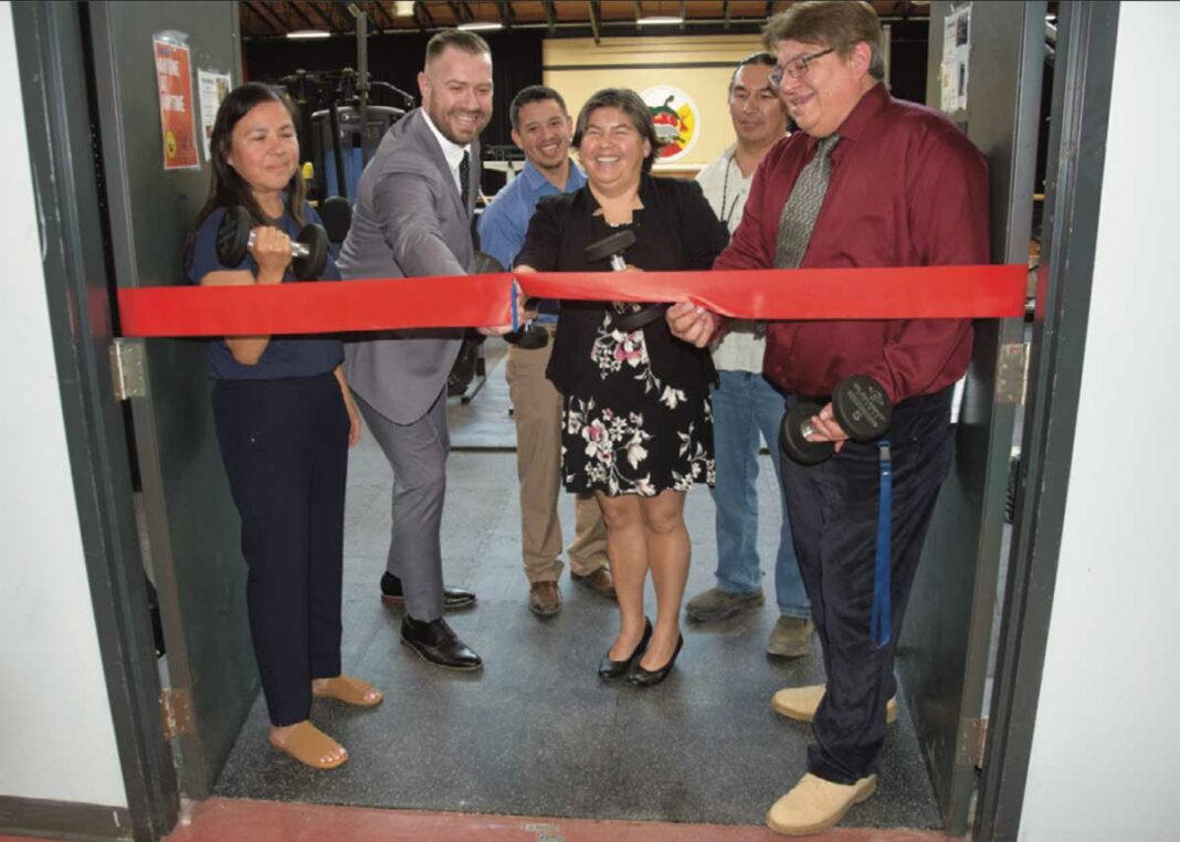 From left, Wiikwemkoong education portfolio holder Marcia Trudeau-Bomberry, teacher/mentor Cameron Beaudry (cutting the ribbon), Maureen Peltier, interim education director and principal Harold Fox open the new weight room at Wiikwemkoong High School.