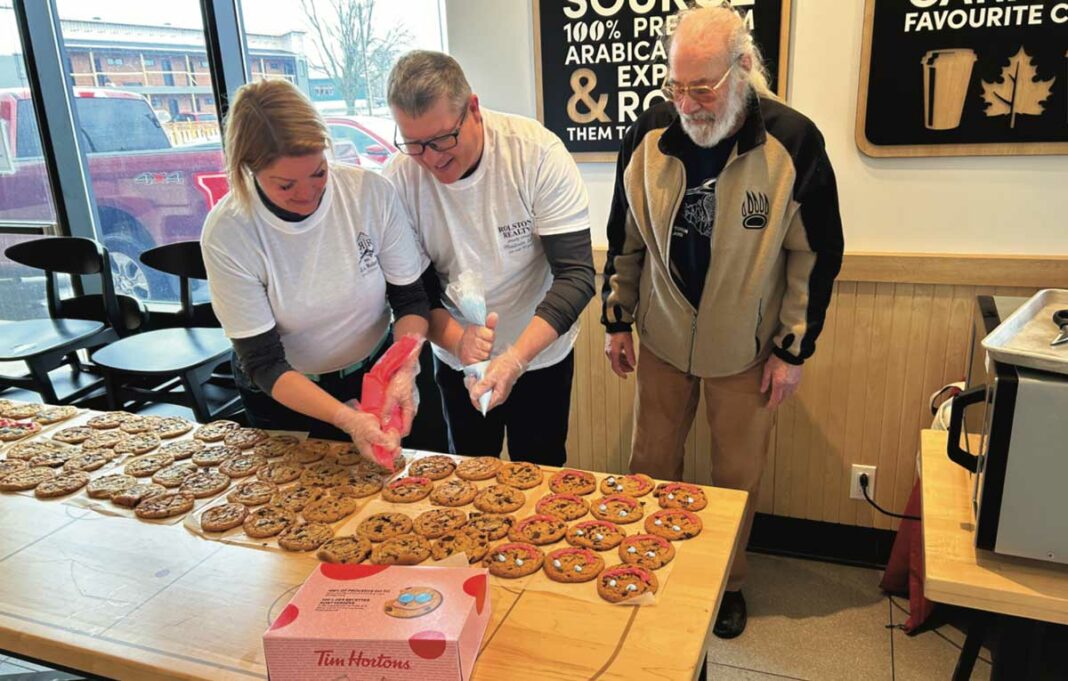 SMILE! Local Food Manitoulin, the organization that provides lower cost fresh food to many Island residents through the Good Food Box program, will be the recipient of the sales of ‘Smile!’ cookies at the Little Current Tim Hortons shop. J.A. Rolston Real Estate Brokerage took on the task of decorating the first day’s Smile! Cookies on Monday, May 1 and the photo shows, from left, Meredith Morris and Steve Rolston adding the classic blue eyes and pink smiles to the first day’s batch under the tutelage of Richard Lathwell, right, board chair of Local Food Manitoulin. The campaign runs the full week, through to the end of Sunday, May 7. Finding cookie decorators like J.A. Rolston Real Estate is the responsibility of Good Food Manitoulin while Tim Hortons bakes the chocolate chip cookies and, as of press time Monday, this Saturday and Sunday were still available for interested parties to help out with decorating. Mr. Lathwell’s phone number is 705-968-0073.