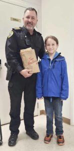 Gavin Eshkakogan, right, presents an officer with the Wiikwemkoong Tribal Police Service with a bag full of Tim Hortons treats recently. Gavin had purchased the donuts using his own funds.